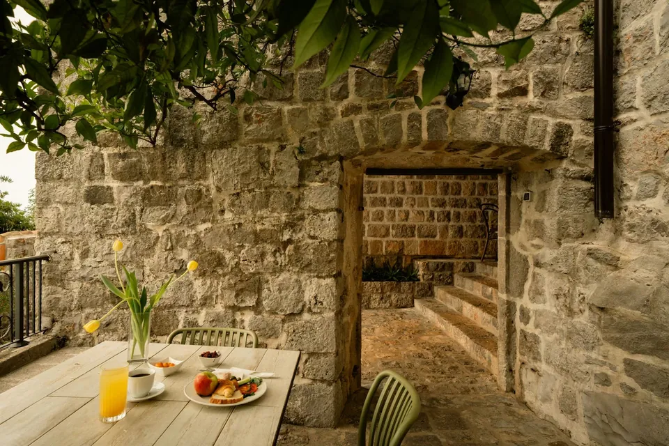 Breakfast table beneath a tree beside stone wall