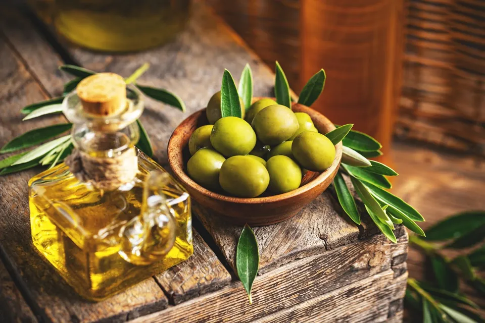 Olive oil bottle and olives with leaves on wooden table