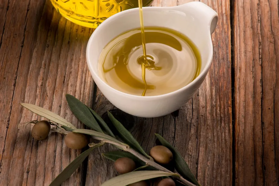 Golden olive oil poured into a white dish beside olives