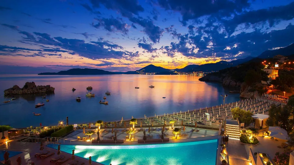 The lit pool and beach at dusk, with Sveti Stefan across the water