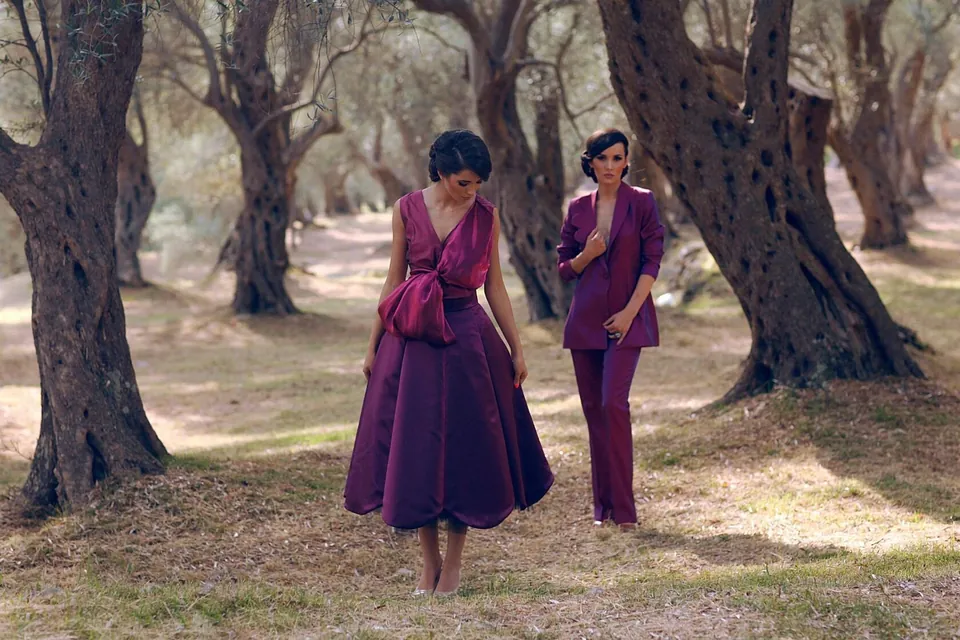 Two models in plum pieces walking through an olive grove