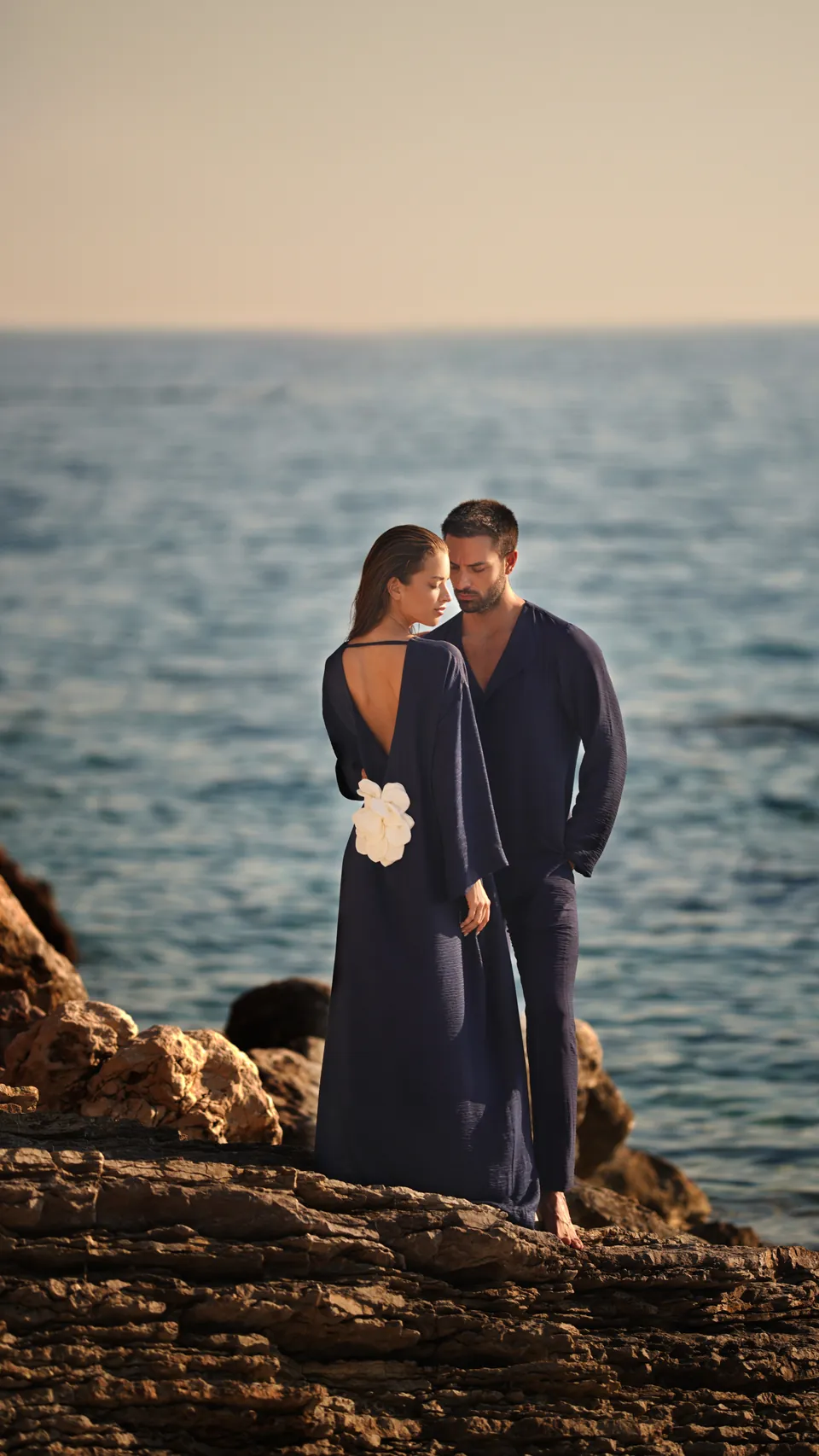 Couple on sea rocks at dusk, navy gown and white flower
