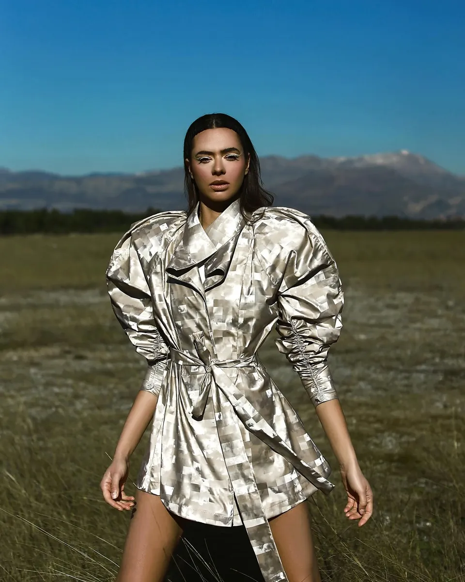 Model in silver jacquard belted jacket in a mountain meadow