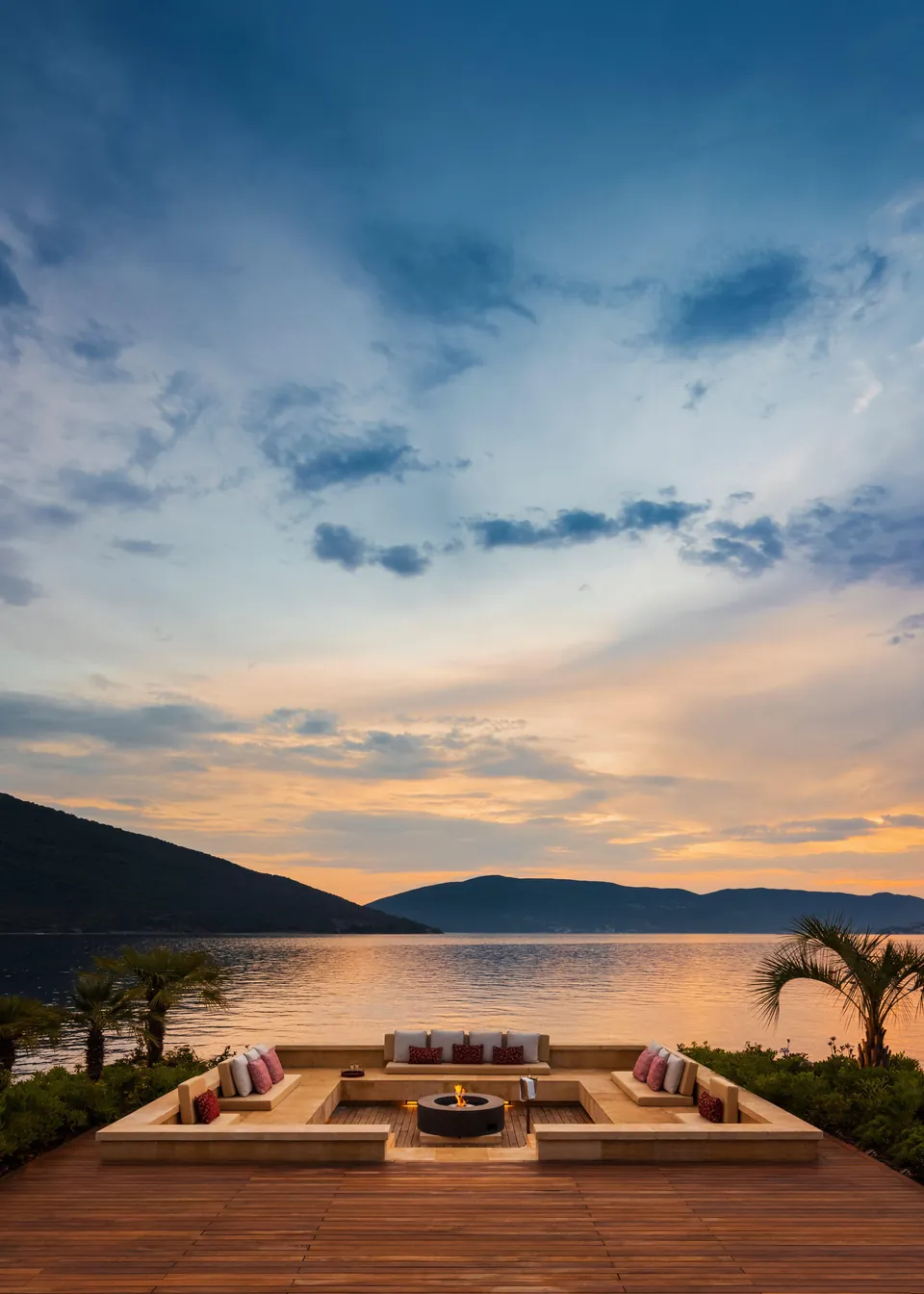 A sunken lounge around a fire pit at the water, with Boka Bay and the hills at sunset