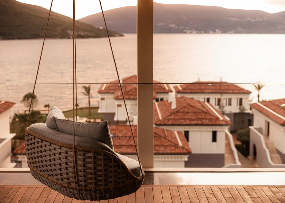 A hanging chair on a terrace above the villa roofs, the bay in the golden hour