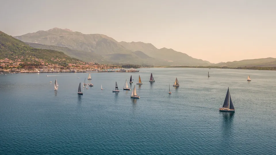 Sailing yachts crossing Boka Bay beneath mountains at dusk