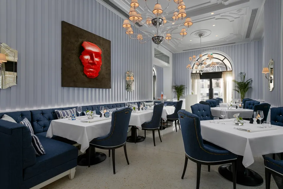 The Murano dining room, blue banquettes and white linen under chandeliers