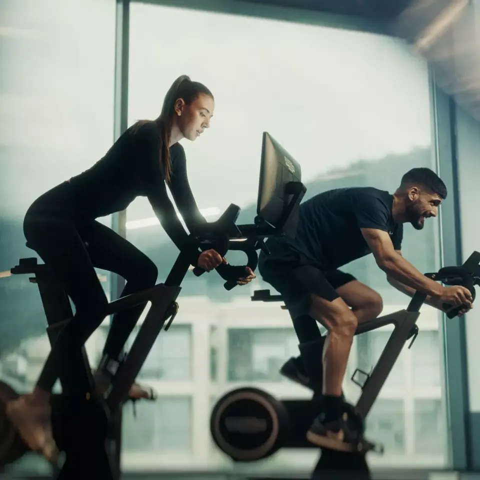 Two guests training on studio bikes in front of the glass wall, with the bay behind