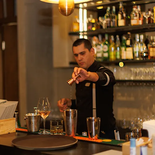 A bartender pouring at the bar, with bottles on the shelves behind