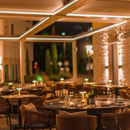 The covered dining room at night, with warm lamps on round tables