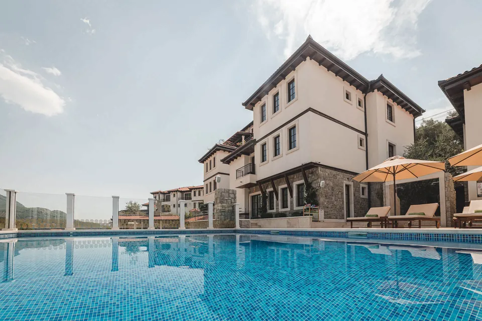 The hotel seen across the pool, stone and white plaster under a deep timber eave, the mountains behind