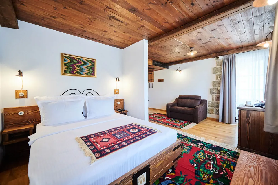 A guest room under a beamed timber ceiling, with white walls and woven Montenegrin rugs