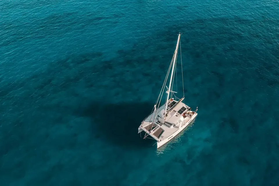 Catamaran anchored on clear turquoise water viewed from above