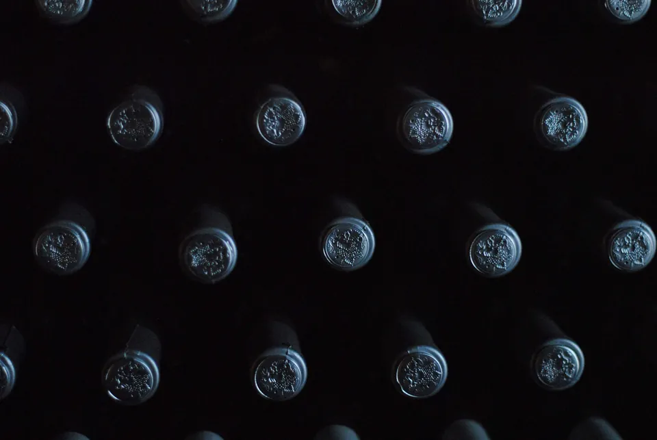 Rows of wax-capped bottle necks resting in a dark cellar